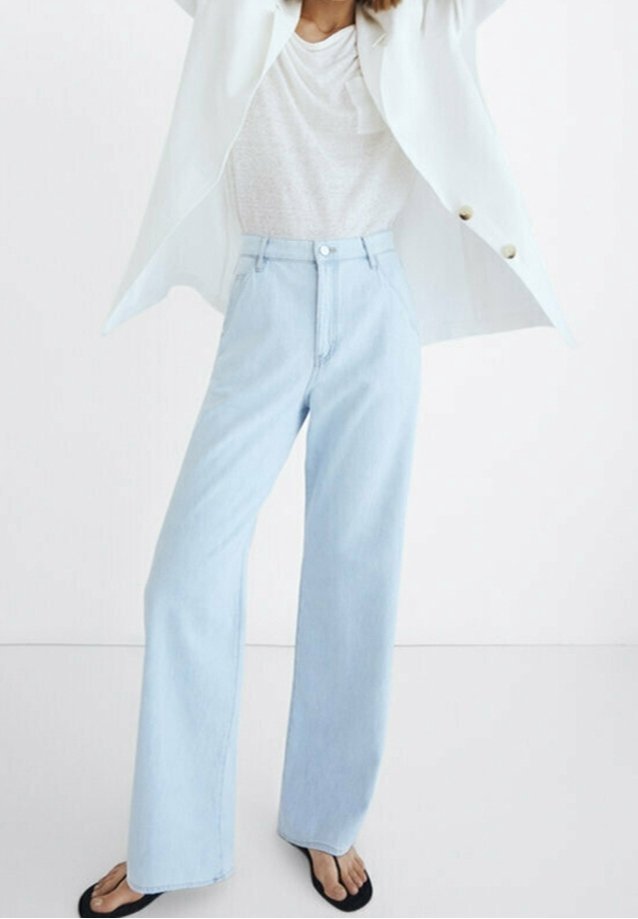 Jean bleu clair taille haute avec une coupe droite, en denim. Assorti à un haut blanc texturé et un blazer blanc. Sandales plates noires.
