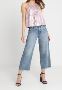 Débardeur à sequins rose à coupe ample, associé à une jupe-culotte en denim bleu clair taille haute avec des bords effilochés, et des talons bleus foncés à brides.