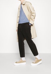 Cappotto beige, maglione blu, pantaloni in velluto a coste neri e sneaker beige con suola bianca. Tessuti morbidi e colori a contrasto.