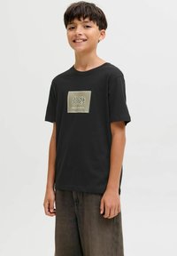 Zwart katoenen T-shirt met korte mouwen en een ronde hals. Geplaatst logo in contrasterende kleuren aan de voorkant, gecombineerd met losse bruine broek.