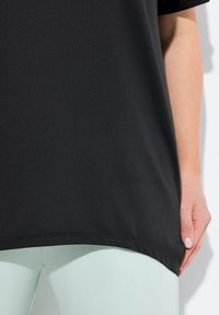 Černý sportovní top s krátkými rukávy, texturovaná tkanina a volný střih. Kombinovaný se světle zelenými legínami, které vytvářejí kontrastní barvy.