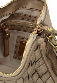 Interno di una borsa a tracolla in pelle beige, dotato di una tasca con zip, foderato in tessuto, con accessori dorati e un design intrecciato testurizzato.