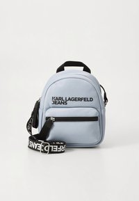 Ljusblå mini-ryggsäck av slätt material. Har ett handtag upptill, justerbar rem, framficka med dragkedja och svart logotyptext.