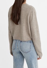 Maglione beige lavorato a maglia con scollatura rotonda, vestibilità corta e orlo a coste, abbinato a jeans in denim azzurro chiaro a vita alta.