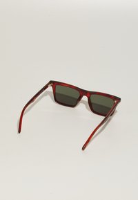 Gafas de sol de plástico tintado rojo con montura rectangular, lentes verdes y patillas delgadas. Presentan acentos de hardware en tono dorado.