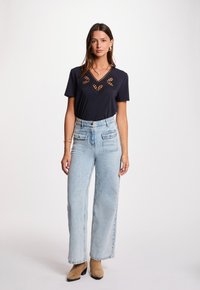 Camiseta navy de cuello en V con patrón de recortes, combinada con jeans de tiro alto en azul claro que cuentan con bolsillos tipo cargo, y botines beige.