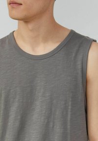 Graues ärmelloses T-Shirt aus weichem Stoff, mit Rundhalsausschnitt und dezentem Logo auf der linken Seite. Sanfte Textur mit leichtem Glanz.