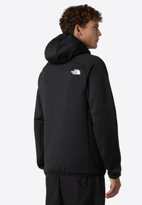 Schwarzer Hoodie aus weichem Material, mit großer Kapuze, seitlichen Taschen und einem weißen Logo auf dem oberen Rücken für das Branding.