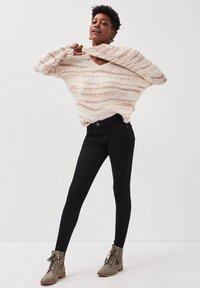 Suéter grueso de punto con escote en v en rayas crema, rosa y durazno. Combinado con jeans skinny negros y botines verde oliva.