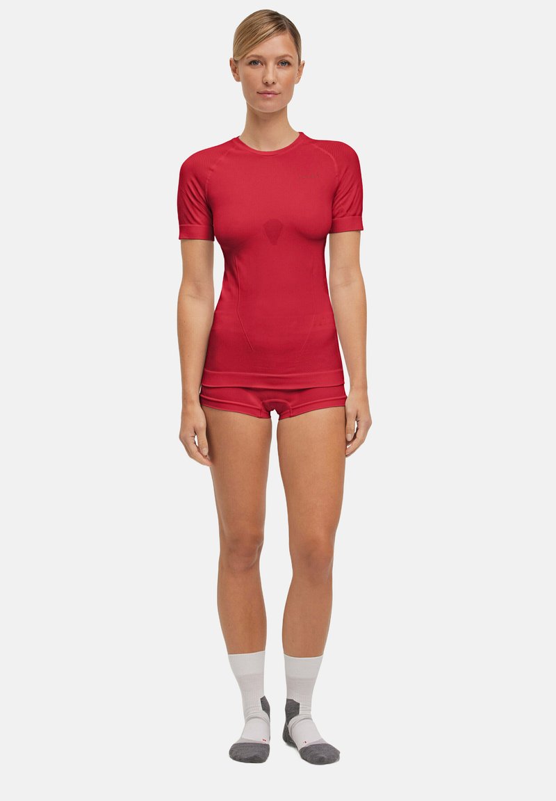 Top attivo rosso con maniche corte e pantaloni aderenti. Realizzato in materiale elastico, presenta una superficie liscia e un design elegante.