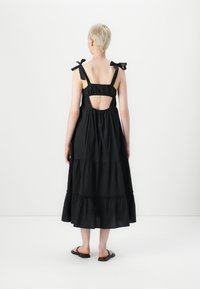 Melnas, daudzslāņu kleitas ar aizmugurē izgriezumu, plāni plecu siksnas, kas sasietas ar bantīm, izgatavota no viegla auduma. Apavi ir vienkāršas melnas sandales.