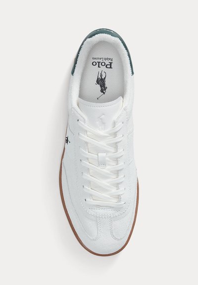 Witte lage sneaker met witte veters, een gestructureerde zool, een groene hieltab, en het zwarte Polo Ralph Lauren-logo binnenin de schoen en aan de zijkant.