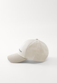 Gorra de béisbol de algodón beige con visera curva, seis agujeros de ventilación y logo bordado en la parte delantera, con un acabado de tela texturada.