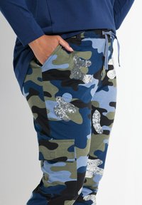 Camo Cargo-Hosen in Blau, Grün und Schwarz mit Paillettenakzenten. Verfügt über Seitentaschen und einen elastischen Bund mit Kordelzug.