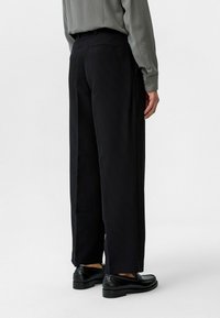 Zwarte pinstripe broek met een losse pasvorm en achterzakken, gecombineerd met een lichtgrijze overhemd met knopen en zwarte schoenen.