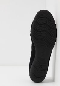 Semelle d'une chaussure noire avec un motif ondulé et le nom de la marque "Gabor" visible, positionnée verticalement sur fond blanc.