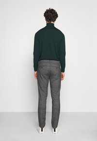 Donkergroene coltrui en grijze geruite broek met een slanke pasvorm en zijzakken. Witte sneakers met zwarte accenten maken de outfit compleet.