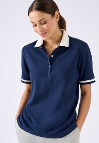Polo shirt bleu marine avec col crème et manches rayées, fabriqué en tissu doux, doté d'une patte de boutonnage à deux boutons et d'un logo discret sur la poitrine.