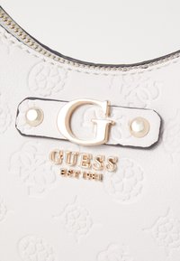 Witte leren handtas met geperste patronen, gouden hardware en een logo-detail. Voorzien van een ritsluiting en decoratieve stiksels langs de rand.