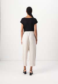 Top nero a maniche corte abbinato a pantaloni a righe di un beige chiaro. I pantaloni hanno una vita elastica e una vestibilità comoda, con design a gamba dritta.