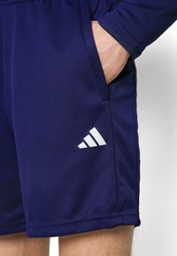 Shorts de sport navy dintr-un material texturat, cu un logo alb Adidas pe partea stângă și buzunare laterale pentru stocare.