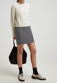 Kermansävyinen palmikkoneulepusero, mustavalkoraidallinen minihame, musta laukku, mustat sukat ja sandaalit, jotka ovat beigenväriset, nauhalliset ja teksturoitupintaiset.