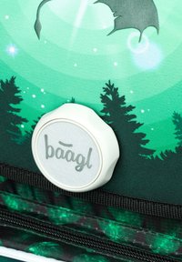 Zielona torba materiałowa z nadrukiem leśnym, okrągły szary guzik z logo "baagl" oraz czarne zamki błyskawiczne na dole.