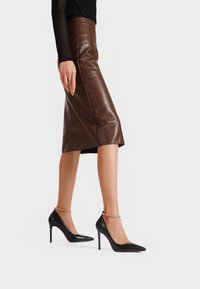 Décolleté nere in pelle con punta affusolata e tacchi a stiletto. Decorate con un sottile cinturino alla caviglia di strass, che mette in evidenza una forma elegante.