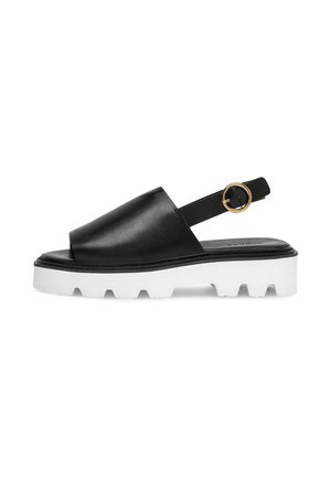 Schwarze Slingback-Sandale aus Leder mit dicker weißer Profilsohle und goldener, runder Schnalle am Knöchelriemen.