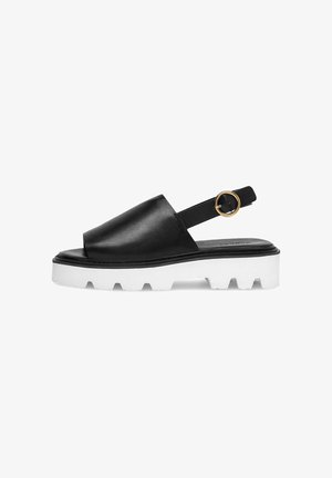 Sandalia negra de cuero con talón descubierto, suela gruesa blanca tipo lug y hebilla redonda dorada en la correa del tobillo.