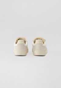 Sko med hvit lær overdel og beige semsket skinn detaljer, med polstret krage, teksturert tunge og "VEJA" logo på hælen.