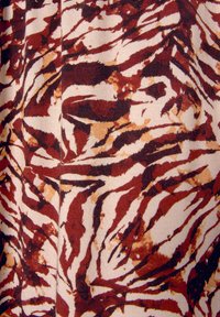 Abstraktes Stoffmuster mit abwechselnden Brauntönen und Creme, verziert mit kräftigen, gewellten Linien, die Tigerstreifen ähneln.