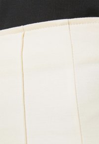 Gros plan sur un panneau en tissu beige avec des coutures verticales et un fond en tissu noir.