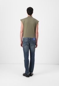 Top sin mangas de color verde oliva combinado con jeans de mezclilla azules. El top presenta un escote redondo; los jeans tienen un diseño clásico de cinco bolsillos con una etiqueta de logo.