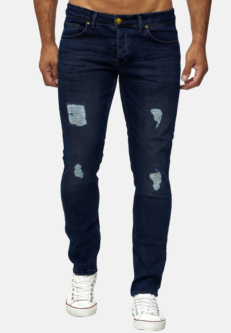 Mørkeblå denim jeans med slidte lapper og lyseblå detaljer. Har en tætsiddende design, fem lomme-stil og lynlås.