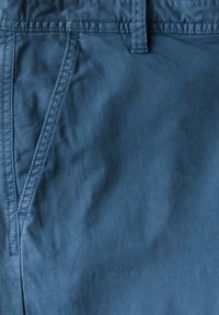 Modrá bavlněná tkanina vystavující hladký povrch, s viditelným šitím, přední kapsou a pasem.