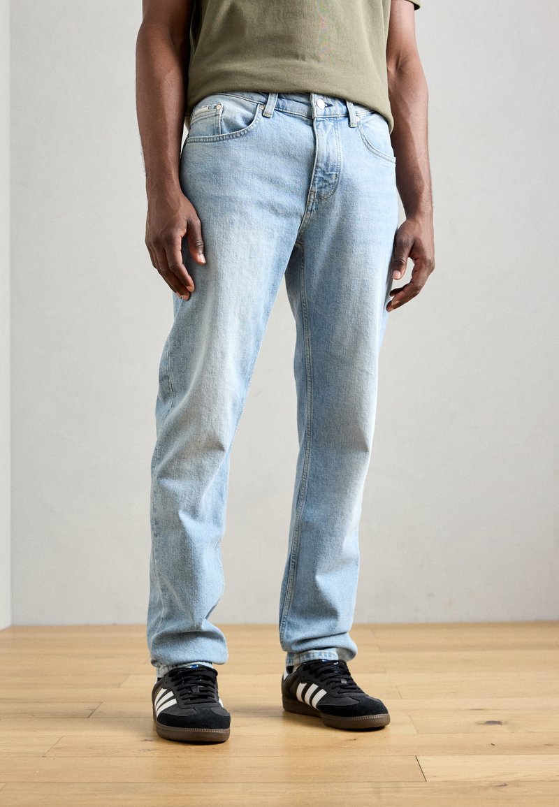 Lys blå denim jeans med rett ben, med knappestolpe, fem lommer og subtil fading, kombinert med svarte treningssko.