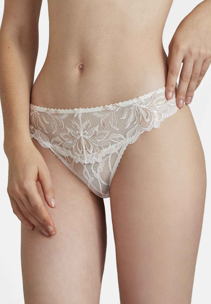 String en dentelle de couleur beige clair avec broderie florale. Doté d'une finition délicate et d'une texture semi-transparente, mettant en valeur les détails complexes du design.