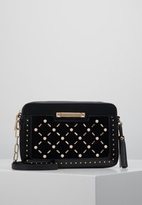 Czarna torba na ramię z teksturowanym wykończeniem, ozdobami w postaci ćwieków, perłowymi detalami oraz złotymi akcentami i odczepianym paskiem.