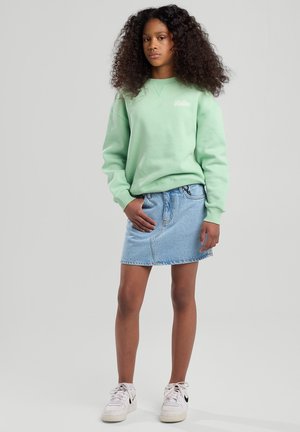 Muntgroene sweatshirt met geribde manchetten, gecombineerd met een lichtblauwe denimrok en witte sneakers met zwarte accenten.