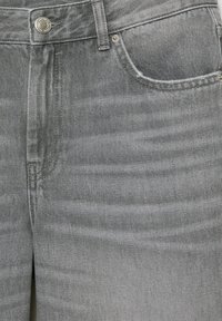 Nærbillede af grå denimjeans, der viser forlomme, bæltestrop, knap og syningsdetaljer på tekstureret stof.