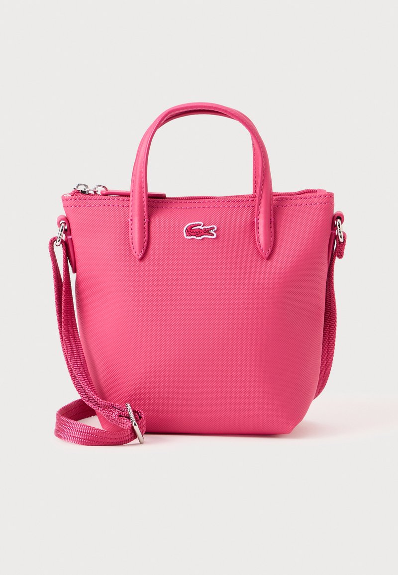 Sac à main synthétique rose avec fermeture éclair, poignées courtes, bandoulière amovible et accent de logo contrastant à l'avant.