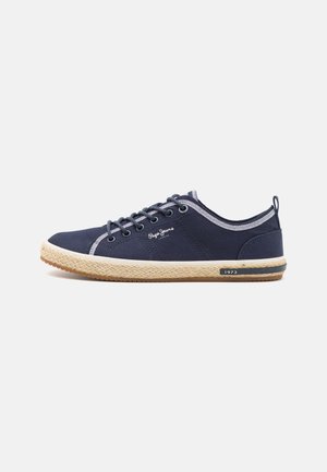Zapatillas de lona azul marino con costuras blancas, punta redonda, parte delantera con cordones y suela envuelta en yute. Cuenta con un lazo trasero y detalle del logo de la marca.