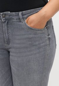 Szürke farmernadrág klasszikus ötpocket kialakítással, enyhén megkopott textúrával és díszöltéssel a zsebeknél.