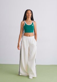 Top cropped verde com acabamento branco e logótipo, combinado com calças largas brancas com riscas laterais pretas. Tecido suave, design atlético.