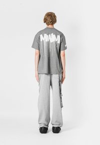 Camiseta de algodón gris con diseño gráfico blanco en la parte posterior, combinada con pantalones de chándal grises que tienen bolsillos laterales y una correa decorativa. Calzado negro.