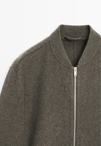 Giubbotto bomber in lana grigia con collo a coste, dotato di una zip argentata e una texture morbida. Progettato con una silhouette semplice e pulita.