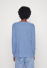 Maglione tricotino azzurro chiaro con maniche lunghe, motivo testurizzato, orlo a costine e scollatura a barchetta, visto di spalle.