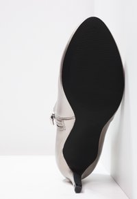 Zapato de tacón alto en plata metálica con punta afilada y suela de goma negra texturizada; presenta un detalle de cremallera lateral.