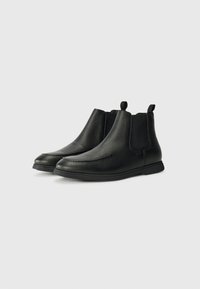 Bottines Chelsea en cuir noir avec une finition texturée, des panneaux latéraux élastiques et des morceaux de tirage en boucle. Design élégant avec une semelle plate en caoutchouc.